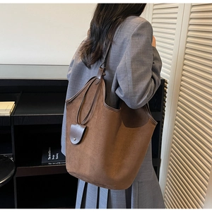 Close-up of brown faux suede tote bag featuring smooth leather straps and bag charm