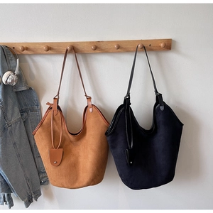 Detail of minimalist suede tote bags in caramel and black on hooks with a denim jacket