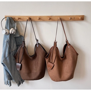 Detail of suede tote bags in dark brown and caramel hanging with minimalist charm