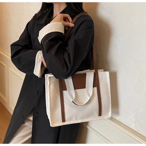Detail of canvas tote bag with brown leather trim and shoulder strap on model