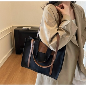 Detail of black canvas tote bag with brown faux leather straps and fashion label