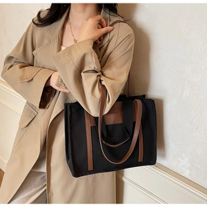 Detail of black canvas tote bag with brown leather trim and fashion engraving