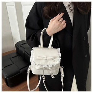 Detail of white ballet-style mini bucket bag with lace trim and bow accent held by model