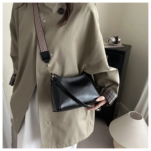 Detail of black patent leather crossbody bag featuring a wide woven geometric shoulder strap