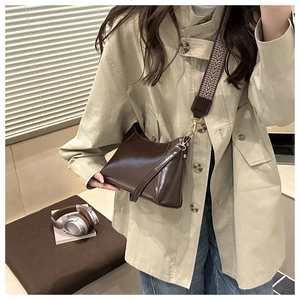 Brown half-moon crossbody bag with patterned wide strap worn by a model in a beige coat