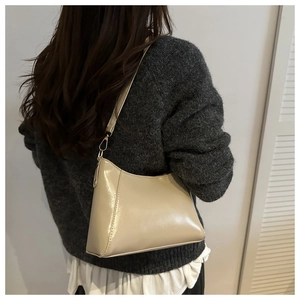 Close-up of cream shoulder bag with glossy PU leather and gold metal hardware hooks