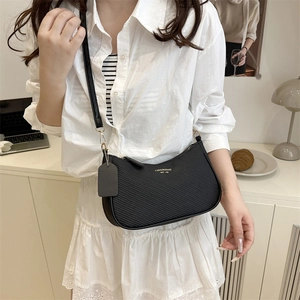 Minimalist black underarm bag with gold logo and shoulder strap worn by a model