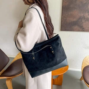 Detail of black suede tote bag with V-quilt texture and gold stud accents on a model
