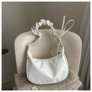 Sac croissant blanc avec anse plissée disposé sur un fauteuil crème élégant