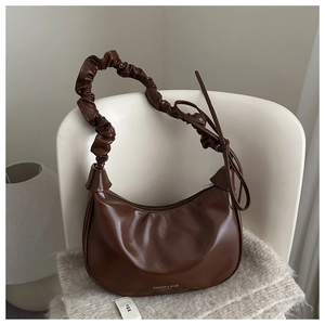 Détail du sac demi-lune marron foncé avec anse plissée et texture cuir lisse