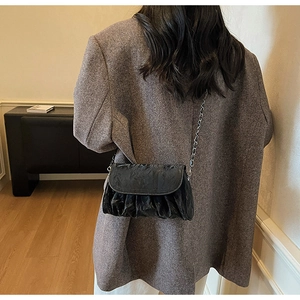 Detail of black pleated cloud bag with silver chain strap worn over a model's shoulder