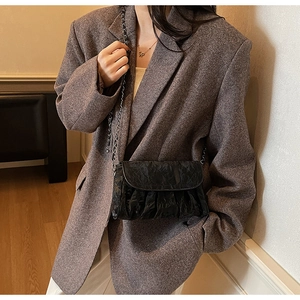 Détail du sac à bandoulière noir plissé avec chaîne argentée sur blazer gris