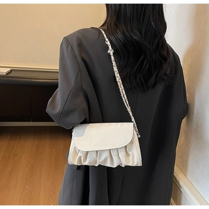Close-up of beige ruched cloud bag with woven chain strap on a grey blazer
