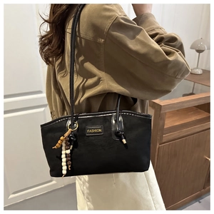 Détail du sac à bandoulière en suédine noire avec pompon en perles de bois et logo de mode