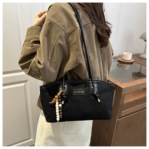 Detail of minimalist black hobo bag with colorful wooden bead charm and gold label