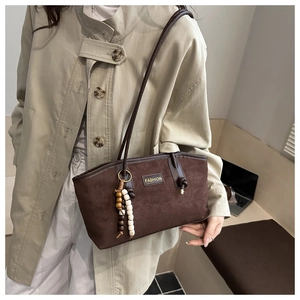 Detail of dark brown suede tote bag with wooden bead pendant and fashion lettering