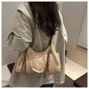Détail du sac hobo en daim beige avec chaîne dorée, perles blanches et fermetures éclair