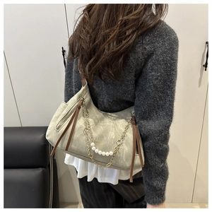 Détail du sac hobo gris-vert avec chaîne dorée et perles porté sur l'épaule du mannequin