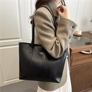 Minimalist black faux leather tote bag with gold lettering shown on shoulder by model