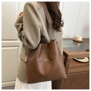 Brown leather tote bag shown on a model with minimalist stitching and exterior pocket