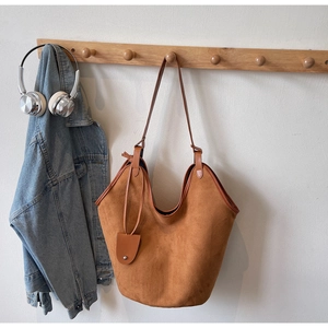 Detail of suede hobo tote bag in tan brown hanging on wooden rack with denim jacket
