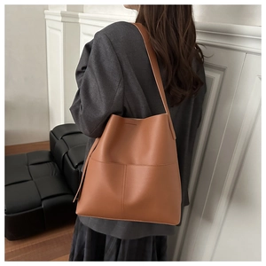 Chic caramel brown leather tote bag worn by a model in a minimalist indoor setting
