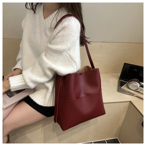 Detail of burgundy leather bucket bag with slim shoulder strap worn by a model