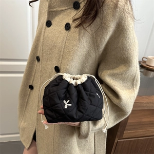 Quilted black drawstring makeup bag with white embroidered bow on minimalist background