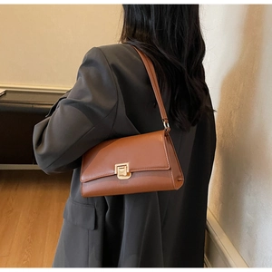 Detail of a brown leather underarm bag featuring a prominent gold metal buckle on a flap
