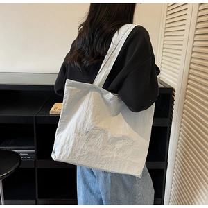 Side view of a light grey canvas tote bag with heart embroidery on a female model