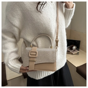Detail of glitter-covered stylish crossbody bag with square buckle on white sweater