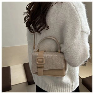 Detail of glitter flap and metal buckle on beige crossbody bag worn with white knit sweater