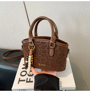 Detail view of brown leopard print crossbody bag with golden logo and beaded pendant