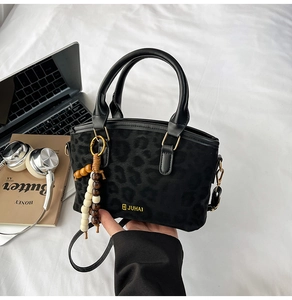 Detail of leopard print handbag with golden logo and wooden beaded tassel charm