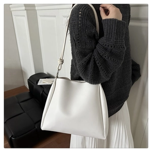 Detailed view of white bucket bag with knotted shoulder strap and side pleat detail