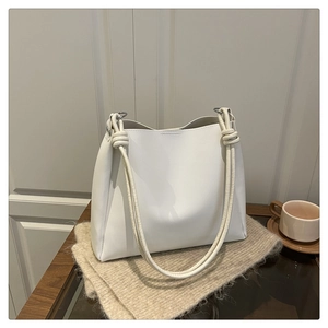 Detail of white PU leather bucket bag with decorative knot straps on beige knit