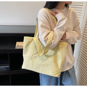 Detailed close-up of white heart embroidery on a minimalist yellow canvas tote bag
