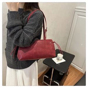 Dunkelrote Vintage-Achseltasche mit Kordelzug-Detail, getragen von einem Model im Raum