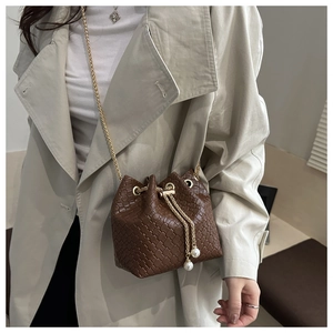 Detail of a brown woven bucket bag with gold chain strap and pearl drawstring accents