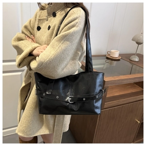 Detail of black glossy shoulder bag featuring silver buckle and metal eyelet accents