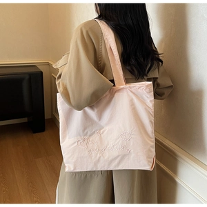 Detail of light pink embroidered tote bag with heart patterns worn over a trench coat