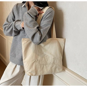 Detail of cream canvas tote bag with subtle embroidery on a grey casual hoodie model