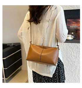 Detailed view of a soft brown leather crossbody bag with vertical stitching on a model