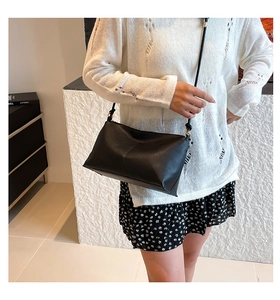 Detail of black minimalist crossbody bag with lychee texture and gold hardware accents