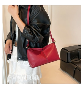 Detail of red leather shoulder bag with vertical stitching and gold hardware on model
