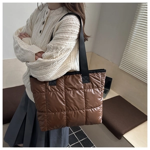 Close-up of brown quilted tote bag with silky texture and wide black shoulder strap