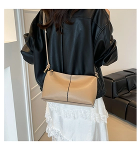 Detail of beige litchi grain bucket bag showing black vertical stitching and slim strap
