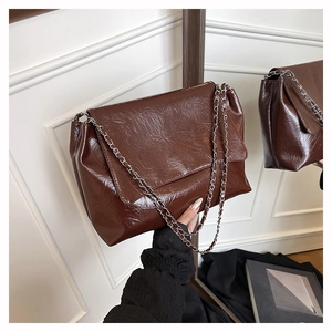 Detailed shot of dark brown wrinkled leather texture and silver chain strap on a tote bag