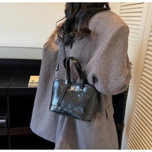 Détail du sac seau noir brillant en cuir avec fermoir métallique sur un blazer gris