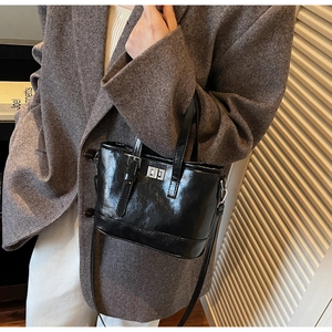 Détail d'un sac seau en cuir verni noir avec fermoir argenté porté sur un blazer chic